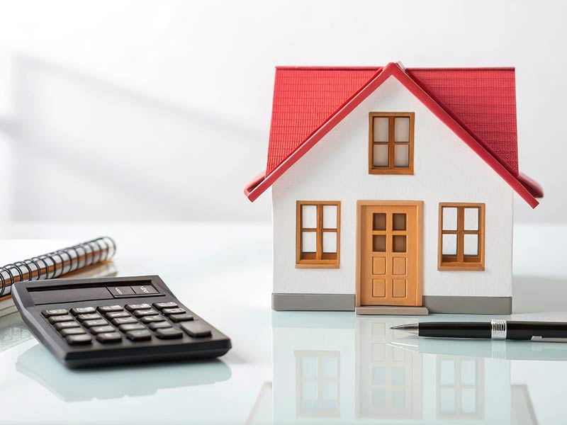 Concept of cost of buying a home, featuring a small model house and a calculator